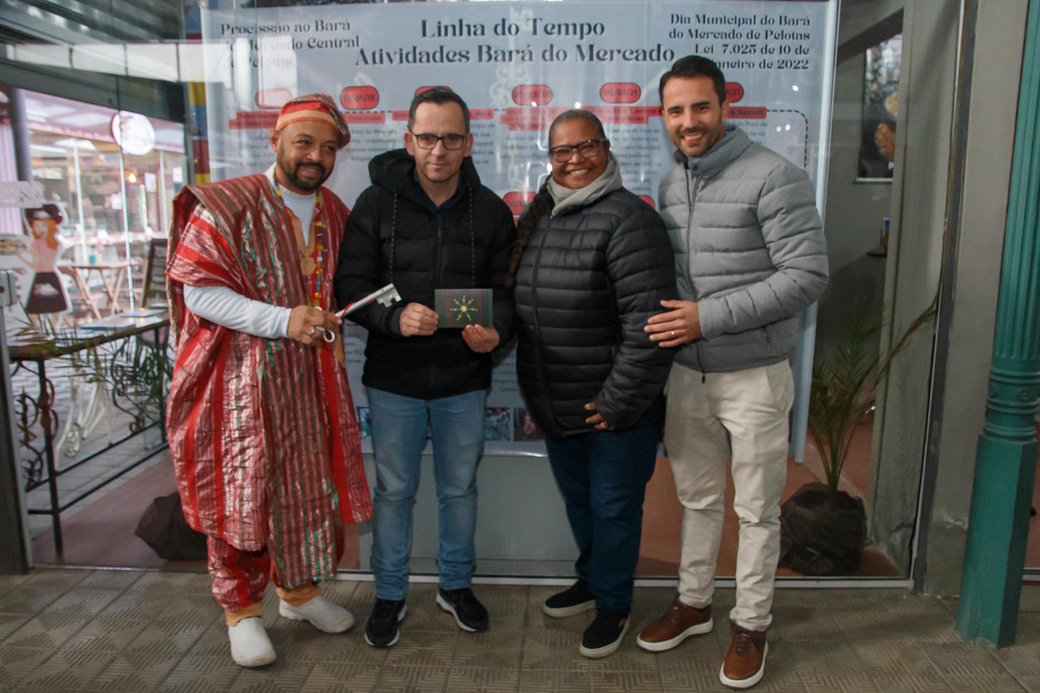 O Postal mostra as chaves e correntes ao centro que representam o elo ao Orixá Bará, e a moldura com a imagem em volta remete a matriz afro diaspórica